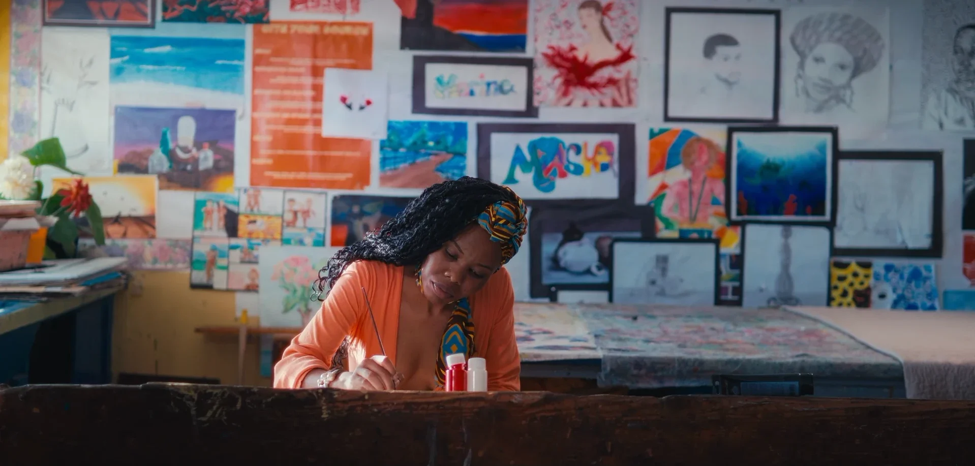 An artist paints alone at a desk in a classroom covered in student artwork in Chiaroscurist (2024), cinematography by George Malcolm Walker