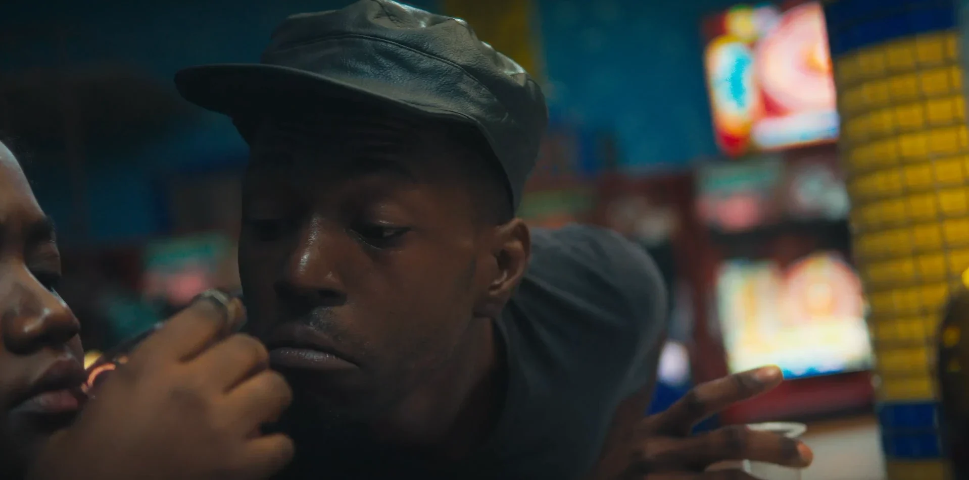 Close-up of a young man in a leather cap in a colourful bar in Chiaroscurist (2024), cinematography by George Malcolm Walker