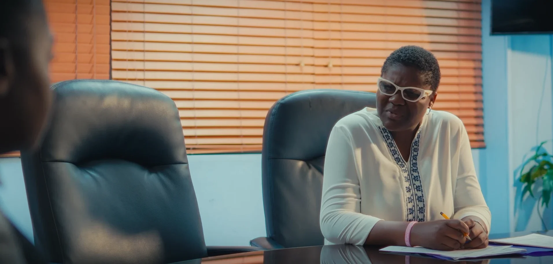 A woman in white glasses frowns across a boardroom table in Chiaroscurist (2024), cinematography by George Malcolm Walker