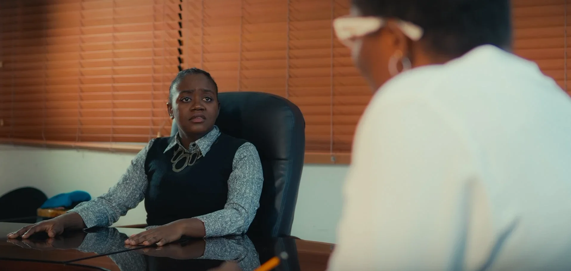 A woman sits at a boardroom table, listening intently in Chiaroscurist (2024), cinematography by George Malcolm Walker