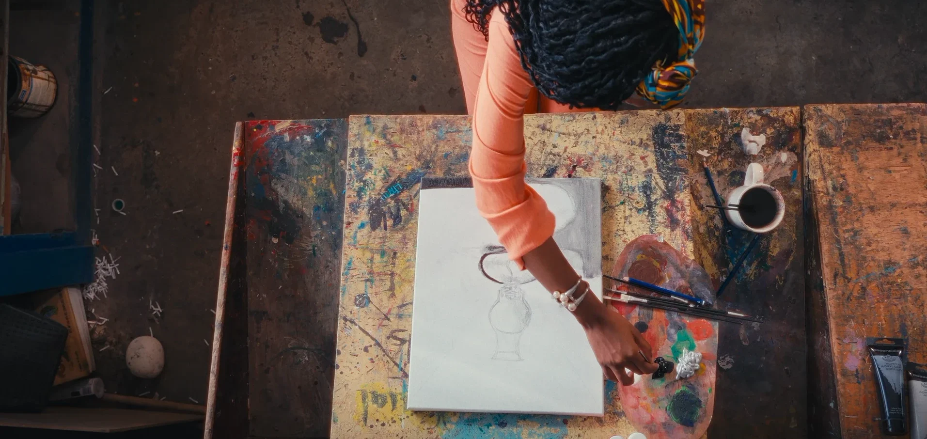 Overhead shot of an artist sketching a vase on canvas at a paint-splattered desk in Chiaroscurist (2024), cinematography by George Malcolm Walker
