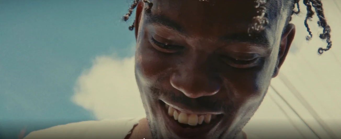 Low-angle close-up of a smiling young man against a blue sky in LICK, a poetic documentary by George Malcolm Walker